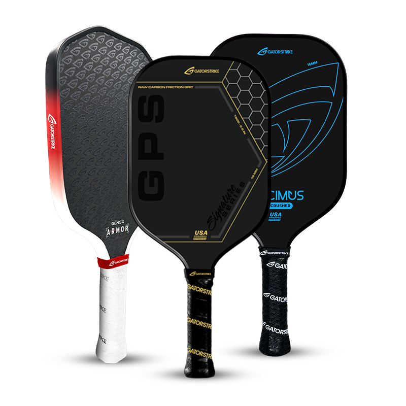 Three pickleball paddles stand upright side by side. Each paddle has a unique design: one is red and gray, one is black with gold text, and one is black with blue accents. All have white handles.