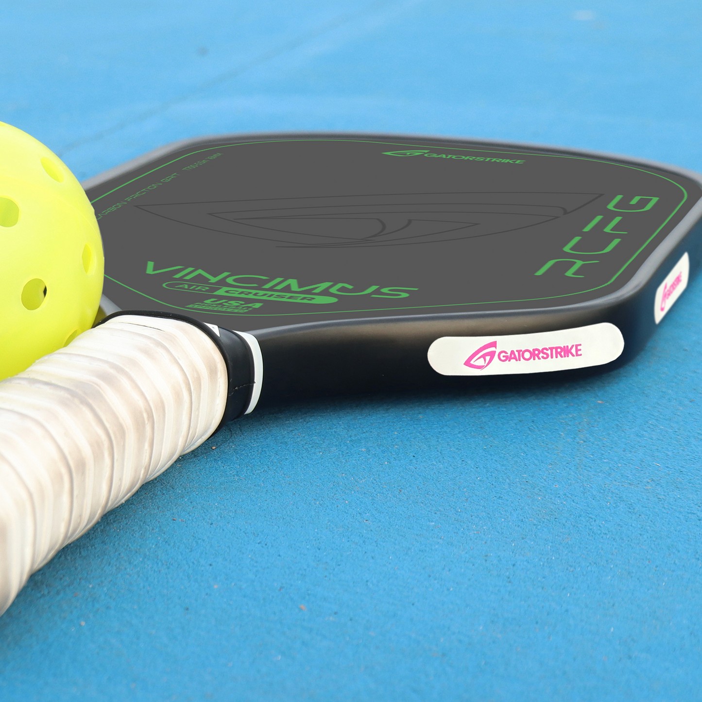 A close-up of Weight Tape 10 Pack - 50 Pack, attached to a black pickleball paddle with green text and a white grip for perfect balance, next to a yellow ball on a bright blue court.