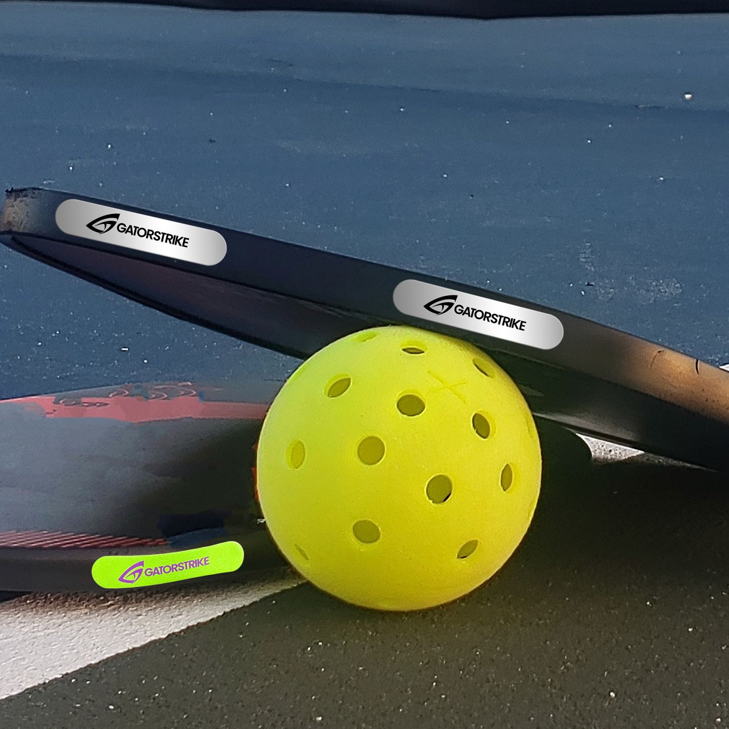 A bright yellow pickleball rests beside black GatorStrike paddles and a third paddle with a neon green logo, all balanced perfectly thanks to the Weight Tape 10 Pack - 50 Pack—a must-have pickleball accessory for every player.